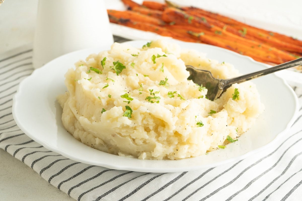 A fowl of cauliflower mashed potatoes on a table with a platter of carrots.