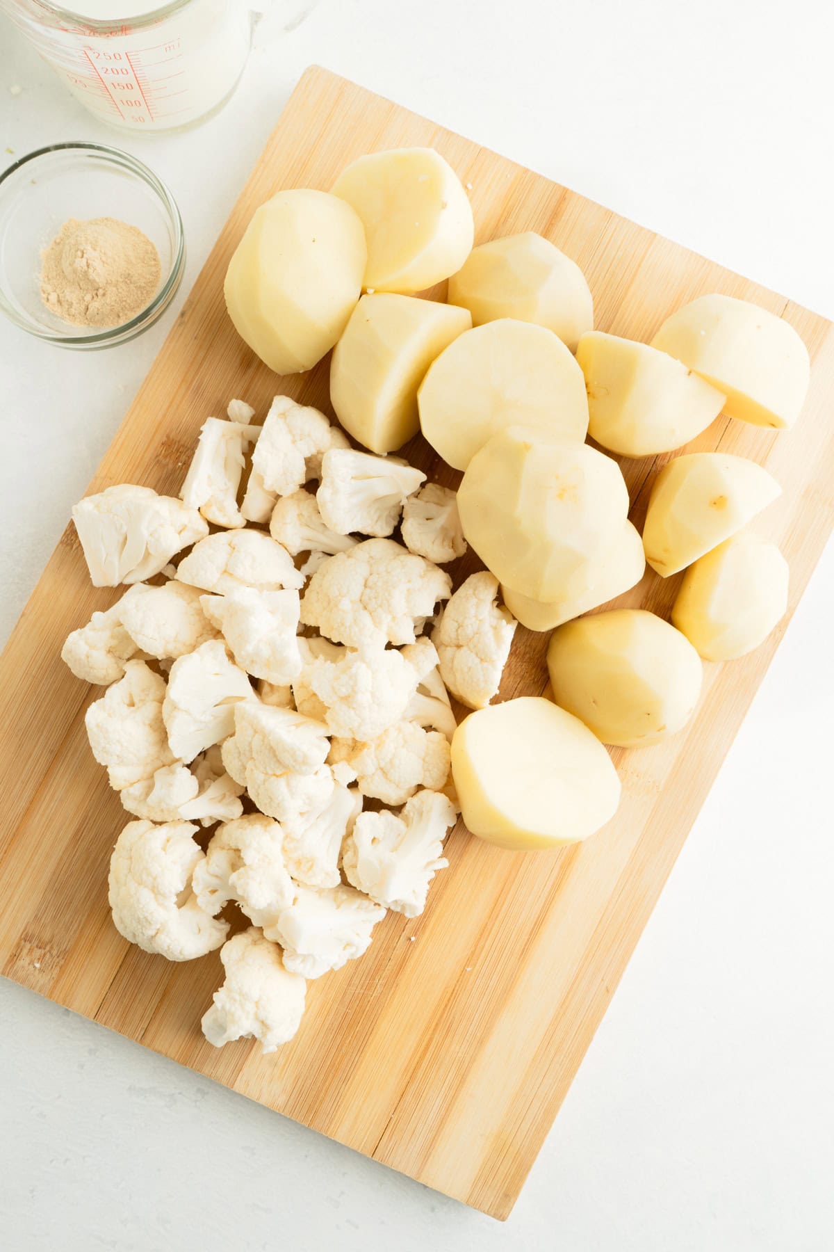 Potatoes and cauliflower florets chopped on a cutting board.
