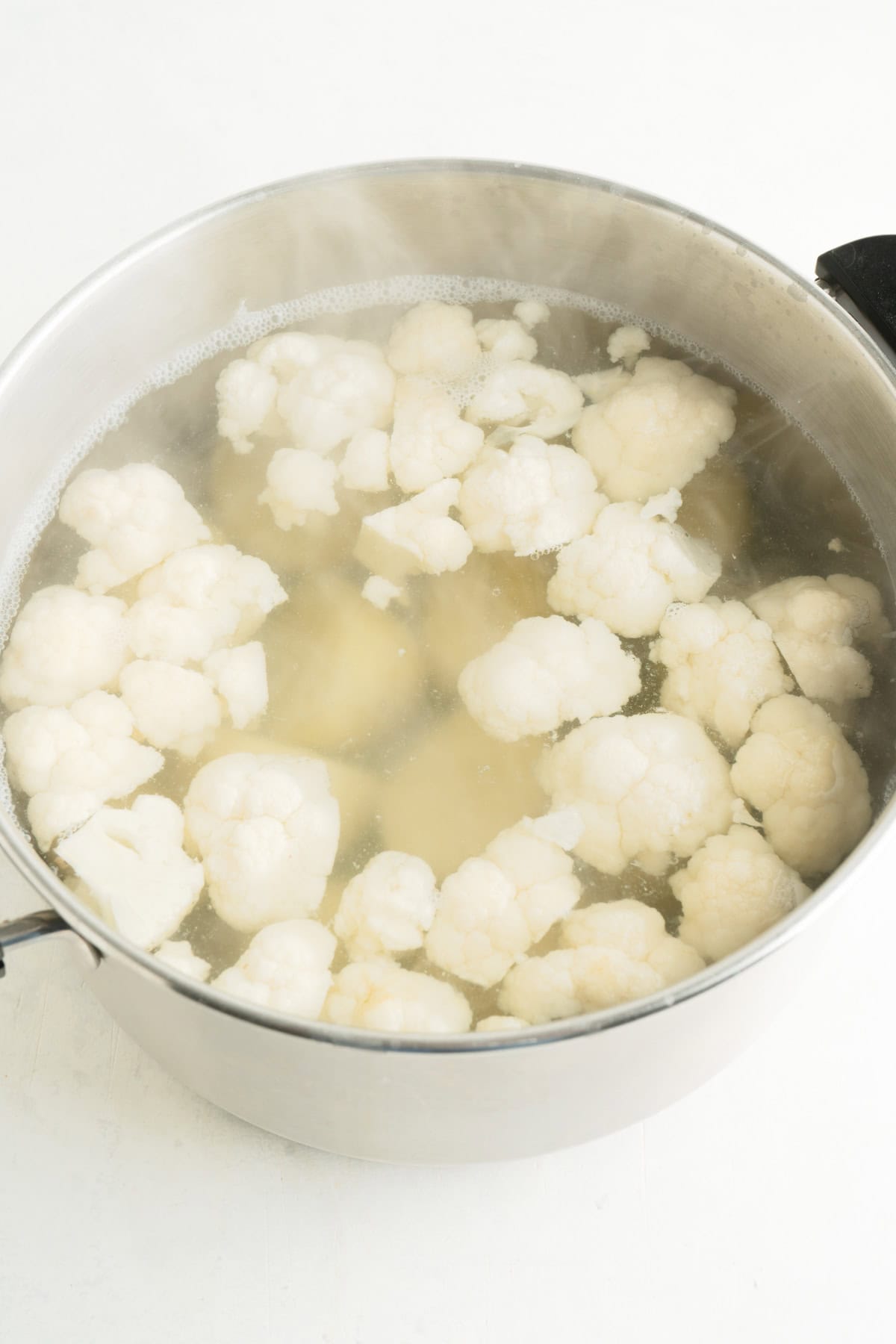 A large pot of water with potatoes and cauliflower.