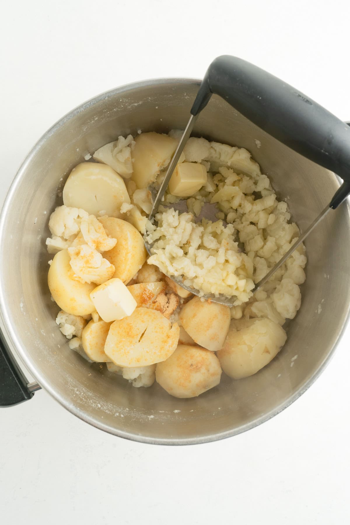 A pot of boiled potatoes and cauliflower being mashed with utter and milk.
