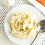A bowl of mashed cauliflower and potatoes on a table with some carrots.