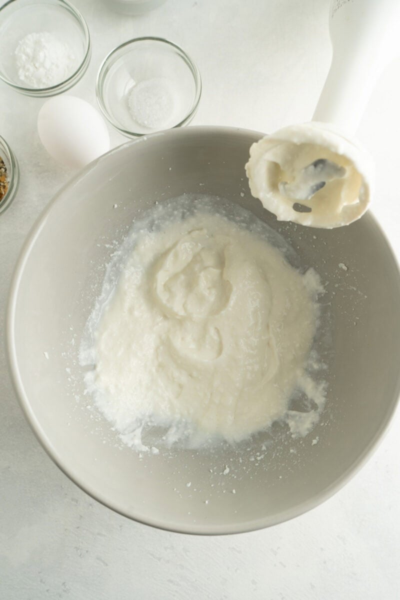 Cottage cheese being blended smooth with an immersion blender on the side of the bowl.
