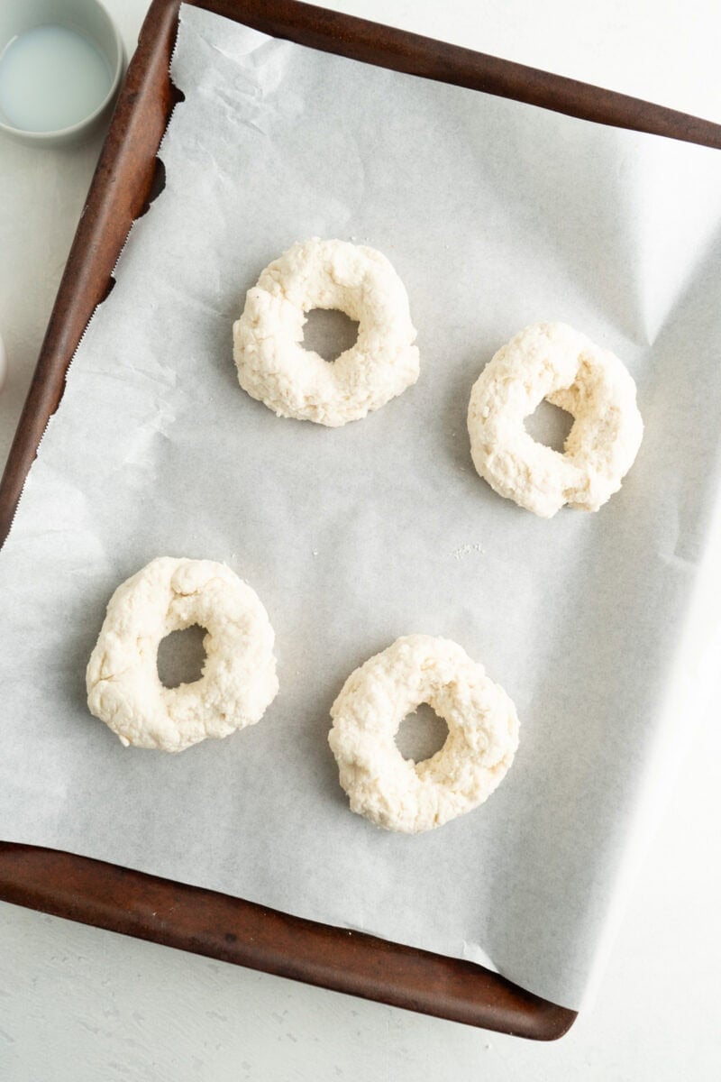 Four unbaked bagels on a baking sheet.