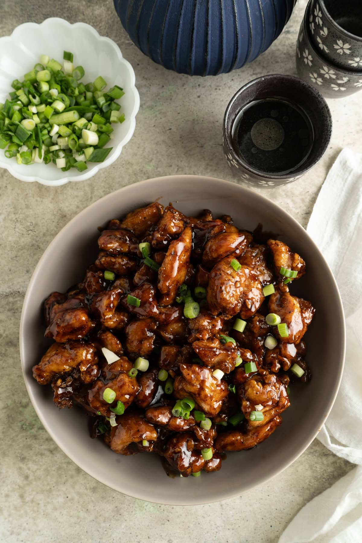 A bowl of honey black pepper chicken on a table with diced green onions.