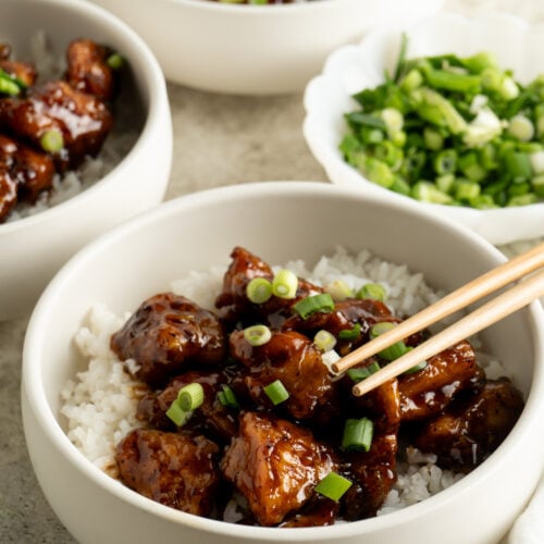 Three bowls of honey black pepper chicken over rice and garnished with green onion.