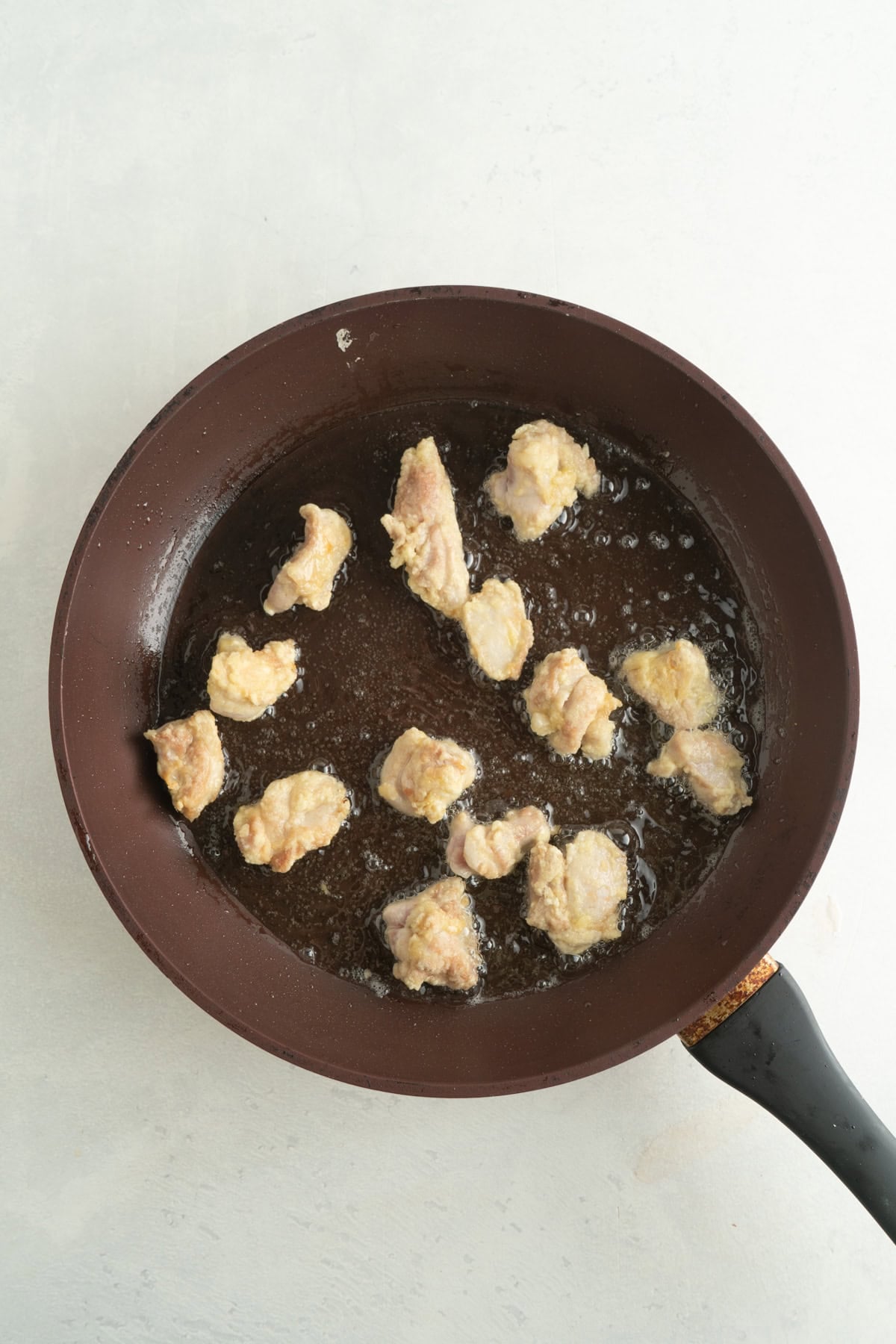 Small pieces of coated chicken being fried in skillet.