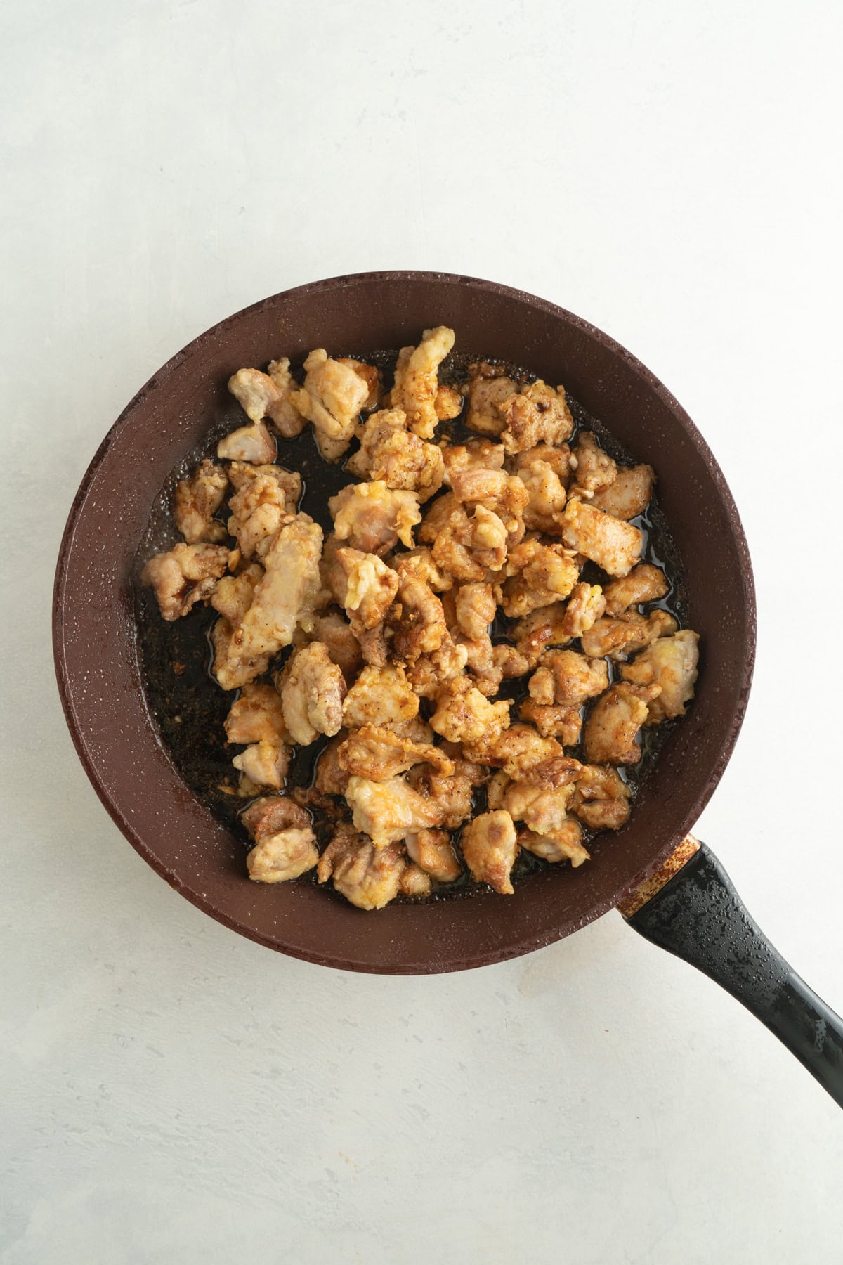 Small pieces of fried chicken in a pan with a honey black pepper sauce.