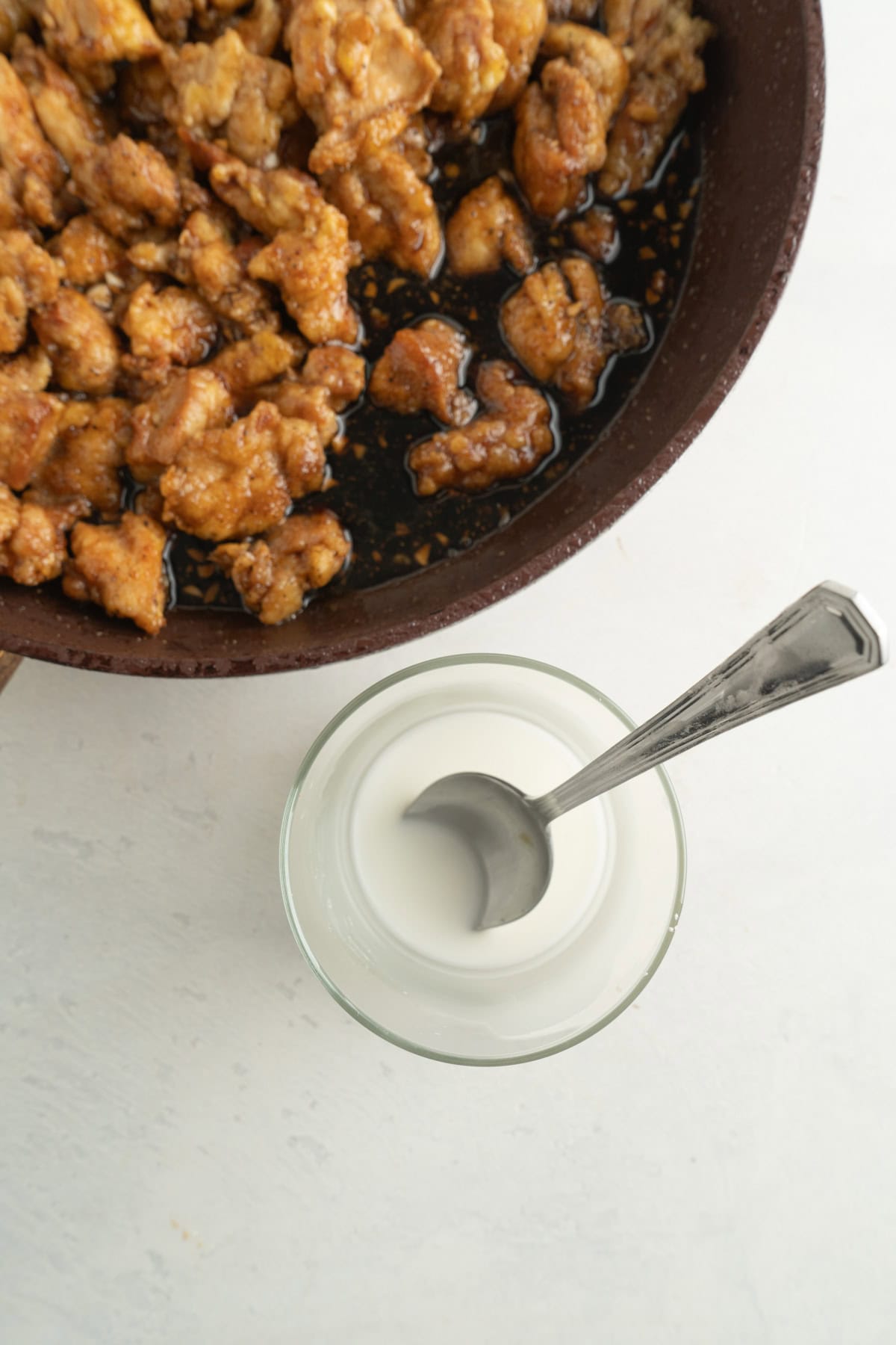 A pan of chicken with a cup filled with a cornstarch slurry nearby.