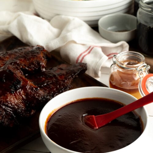 A bowl of memphis-style BBQ sauce in a bowl beside a stack of ribs.