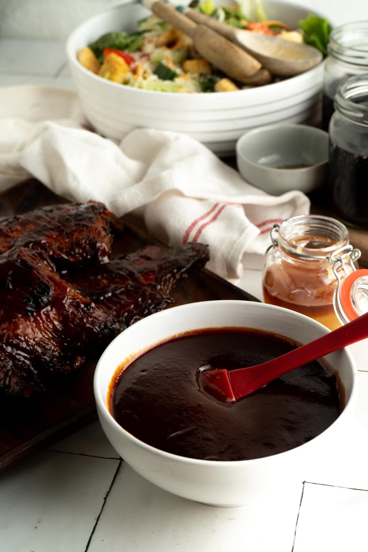 A bowl of memphis-style BBQ sauce in a bowl beside a stack of ribs.