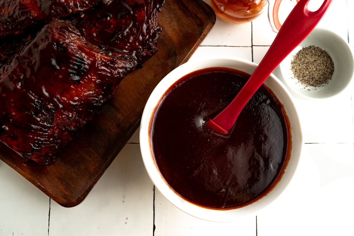A Memphis Barbecue Sauce in a bowl with a basting brush and ribs nearby.