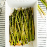 A dish filled with parmesan roasted asparagus on top of a striped dish cloth.