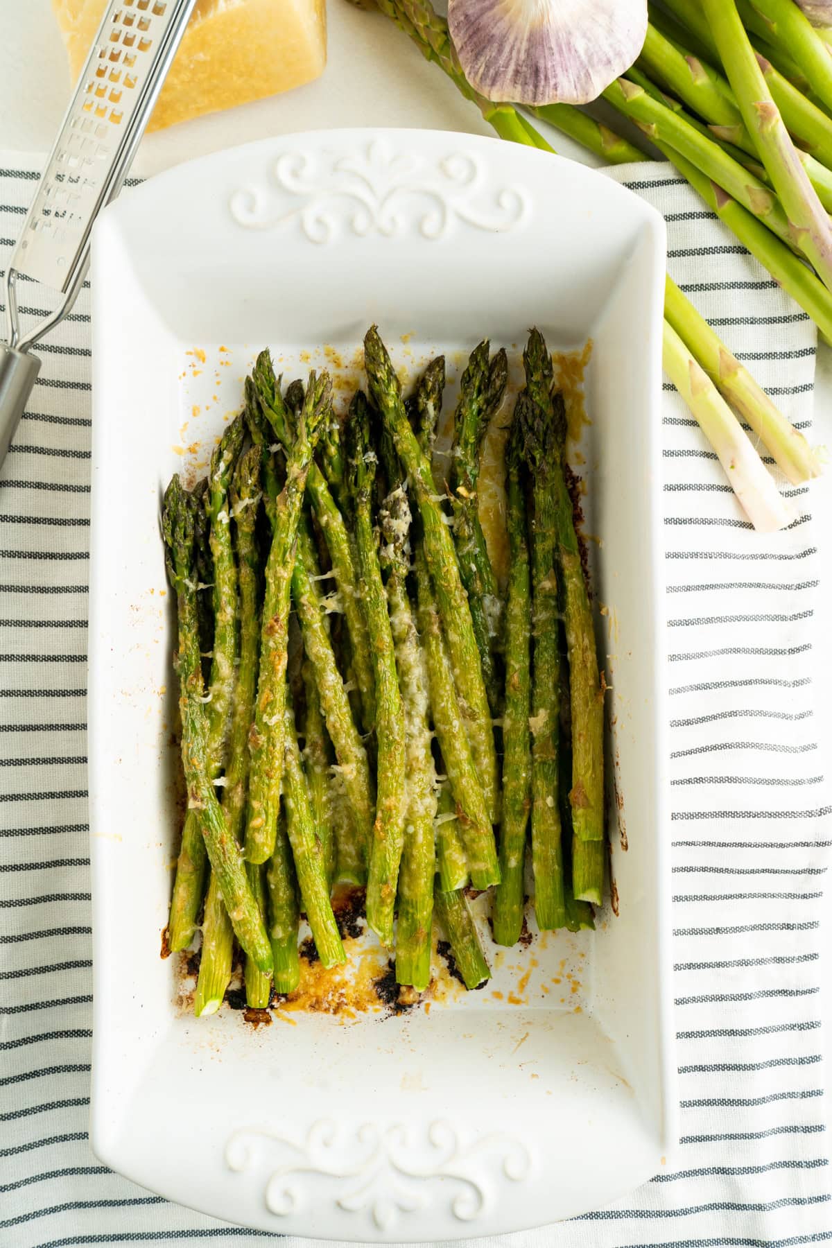 A dish filled with parmesan roasted asparagus on top of a striped dish cloth.