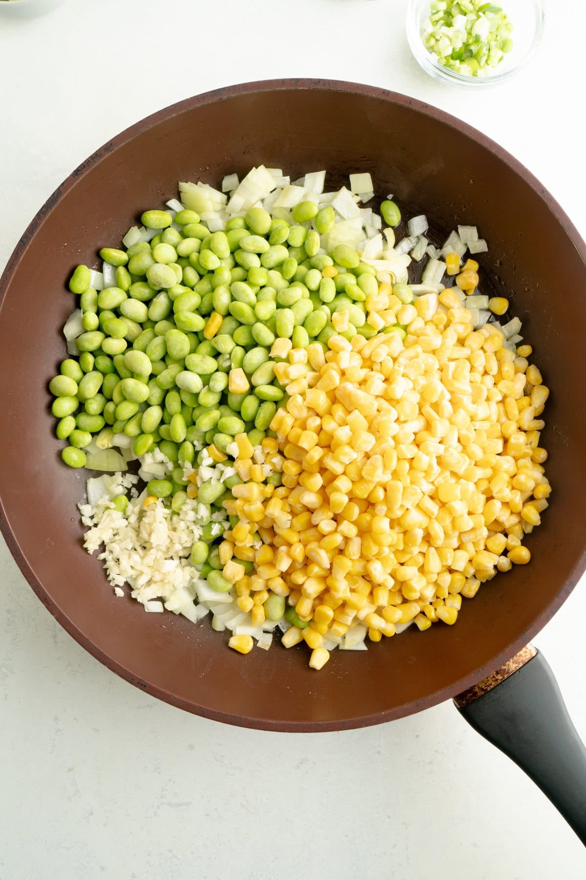 Edamame, corn and garlic added to a pan.