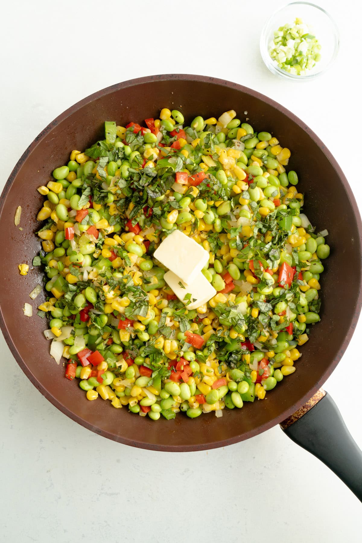 Succotash in a pan with chopped basil and pats of butter.