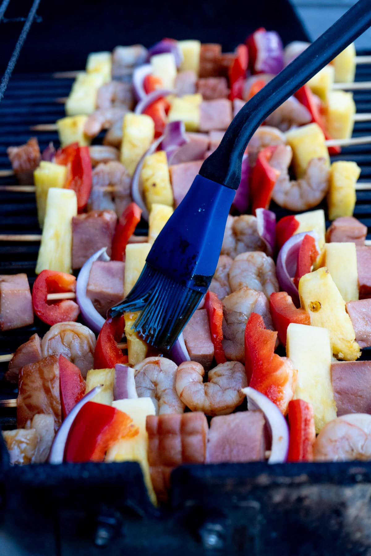Shrimp skewers with ham being basted on a grill.