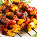 A plate of pineapple shrimp skewers with ham on top of palm leaves.