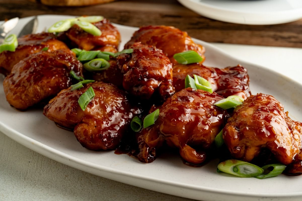 A platter of sticky honey garlic chicken topped with green onion.