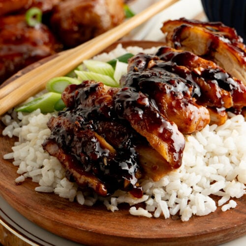 A plate of sliced sticky honey garlic chicken on rice with chopsticks.