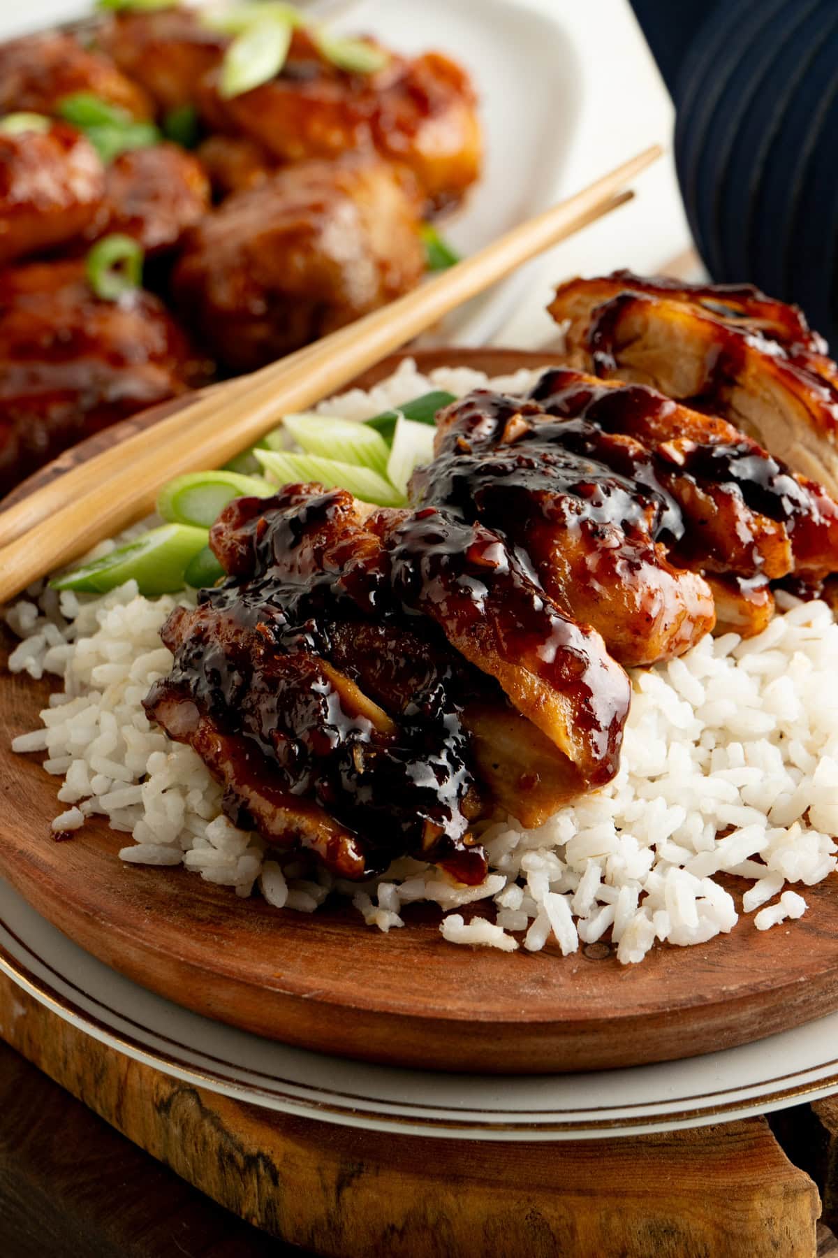 A plate of sliced sticky honey garlic chicken on rice with chopsticks.