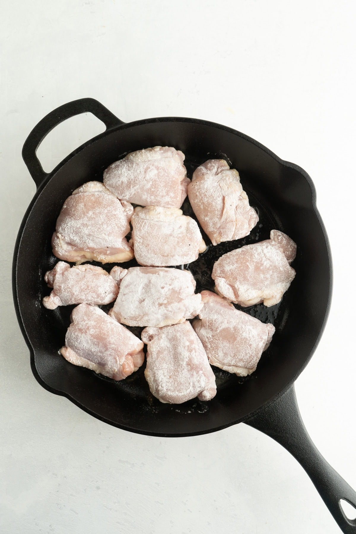 Floured chicken thighs in a cast iron pan.