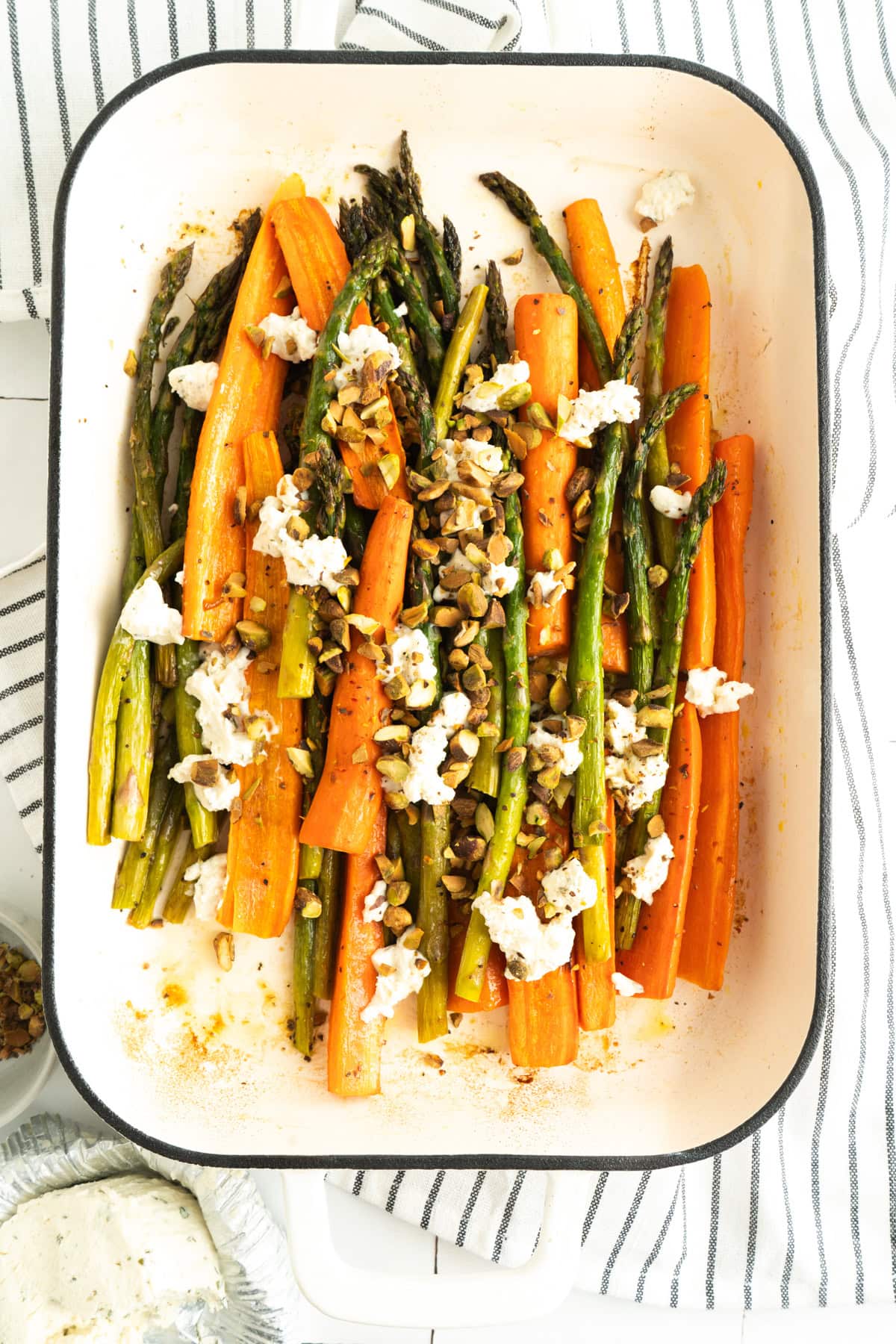 Roasted asparagus and carrots in a pan with crumbled cheese and nuts.
