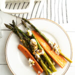 A plate of roasted carrots and asparagus topped with crumbled cheese and pistachios.