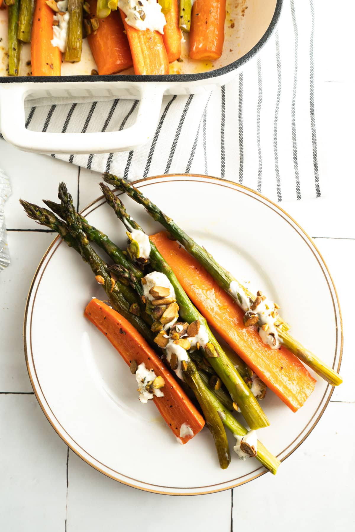 A plate of roasted carrots and asparagus topped with crumbled cheese and pistachios.