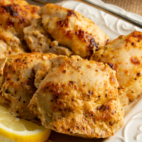 Close up of a Greek marinated chicken thigh with a slice of lemon.