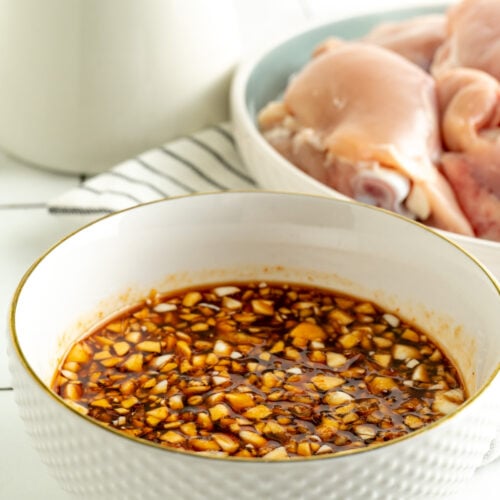 A bowl of honey sriracha sauce next to a plate of raw chicken.