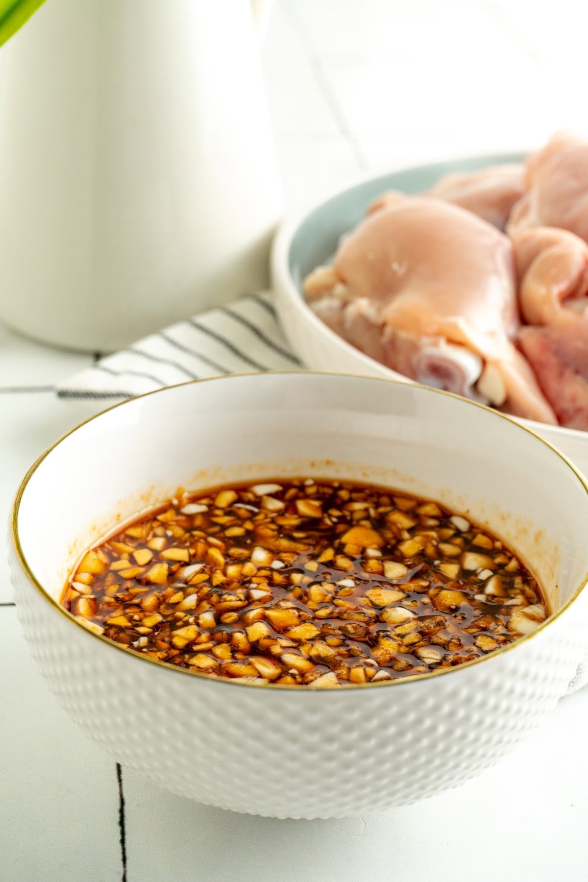 A bowl of honey sriracha sauce next to a plate of raw chicken.