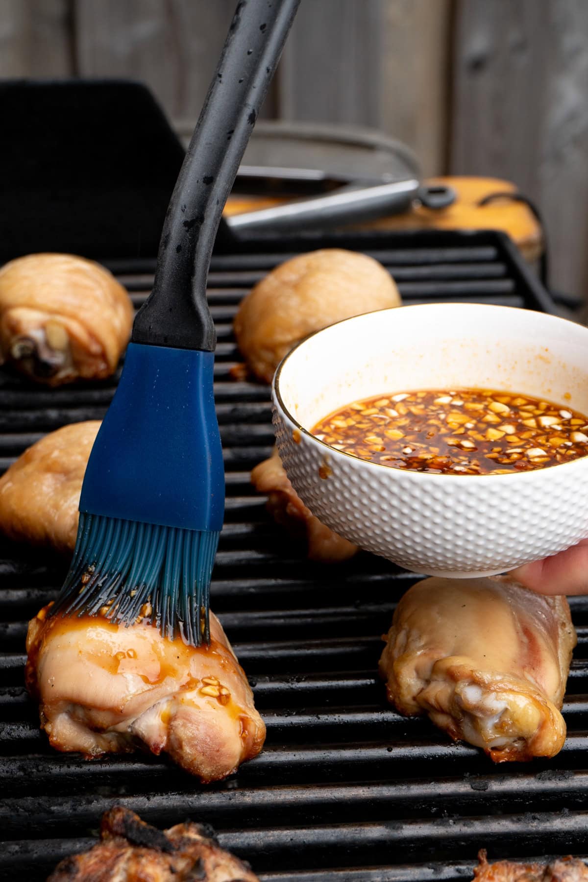 Chicken on a grill being basted with sauce.