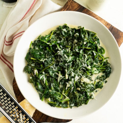A bowl of creamed spinach and a brick of parmesan nearby.