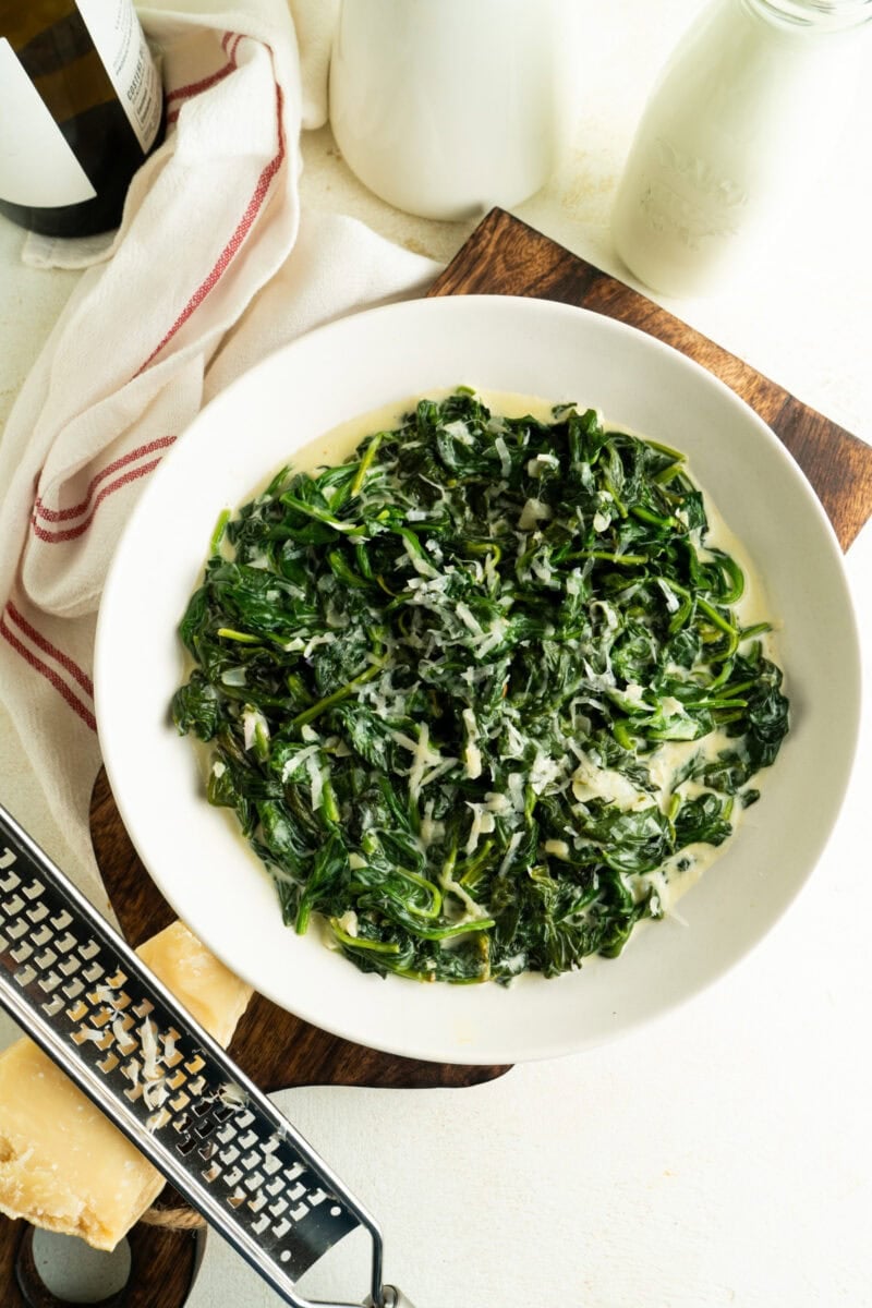 A bowl of creamed spinach and a brick of parmesan nearby.