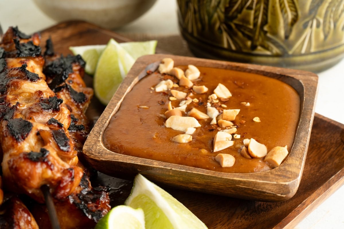 Peanut Satay Sauce in a wood dish on a platter with skewers.