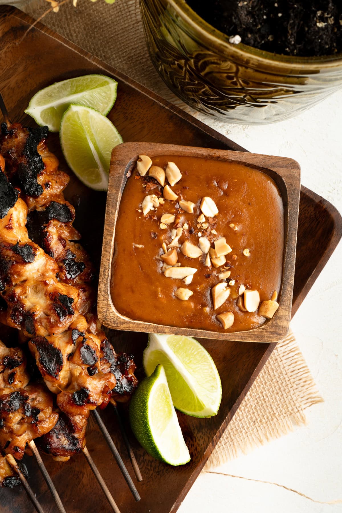 An overhead shot of peanut sauce in a wood bowl with skewers on a plate.