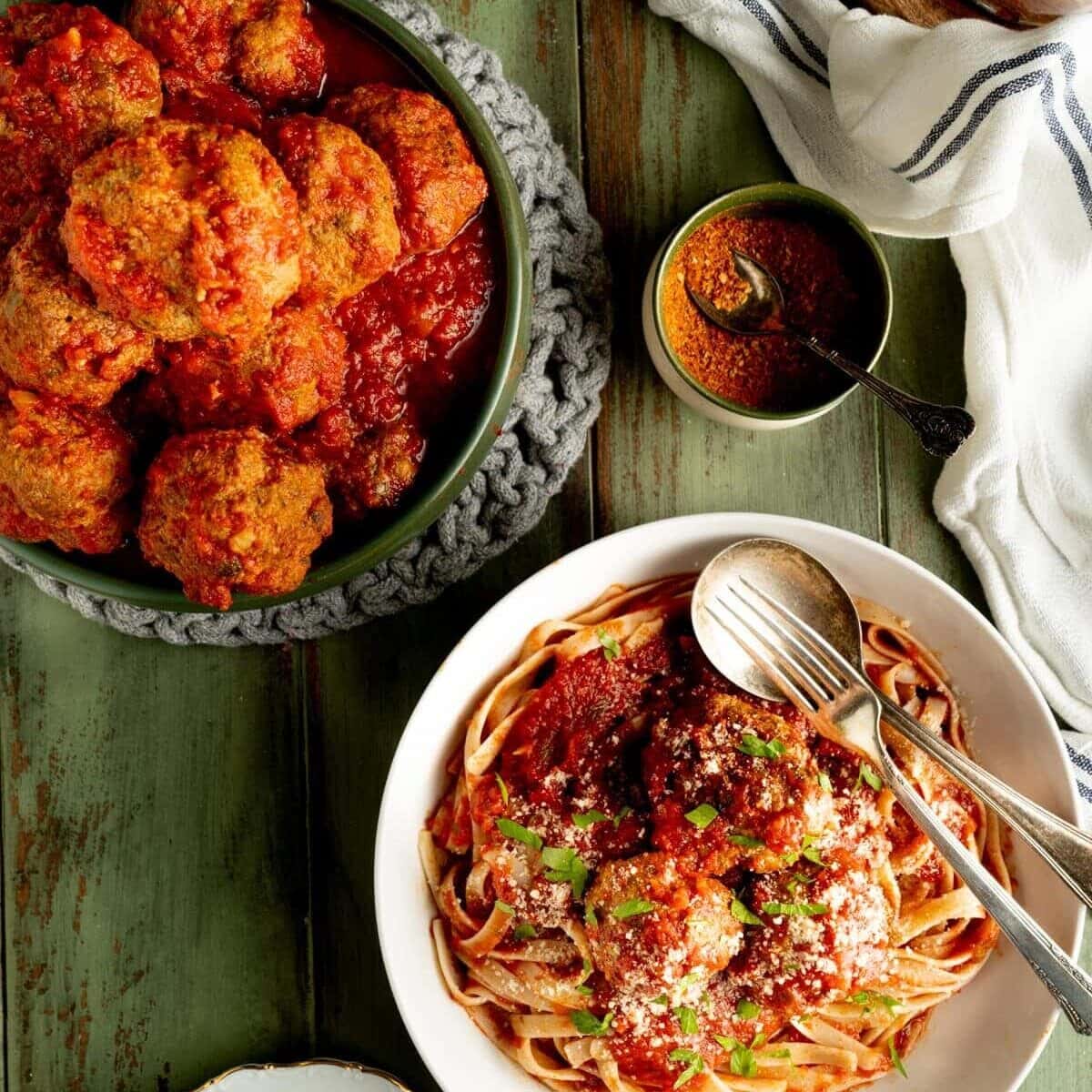 The best Italian meatballs shown on a table with pasta and hot peppers.