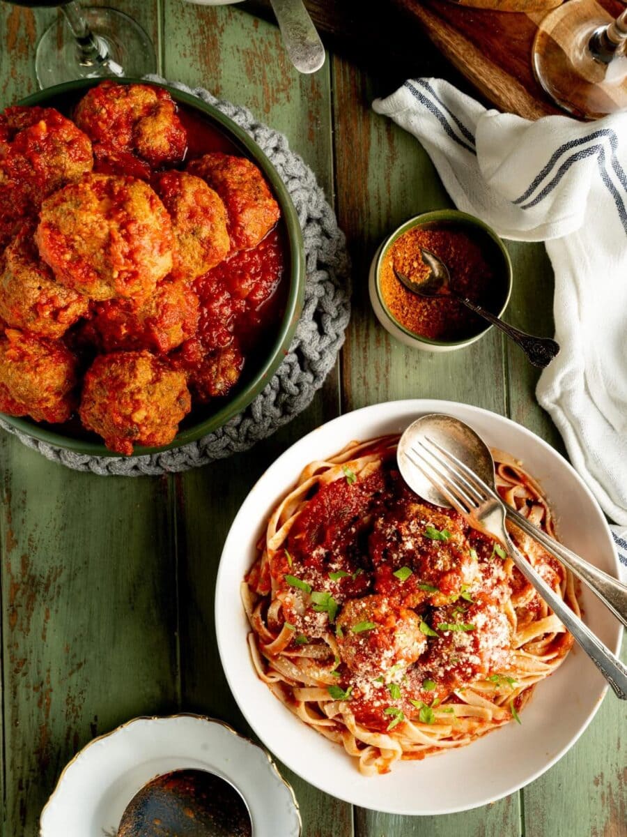 The best Italian meatballs shown on a table with pasta and hot peppers.