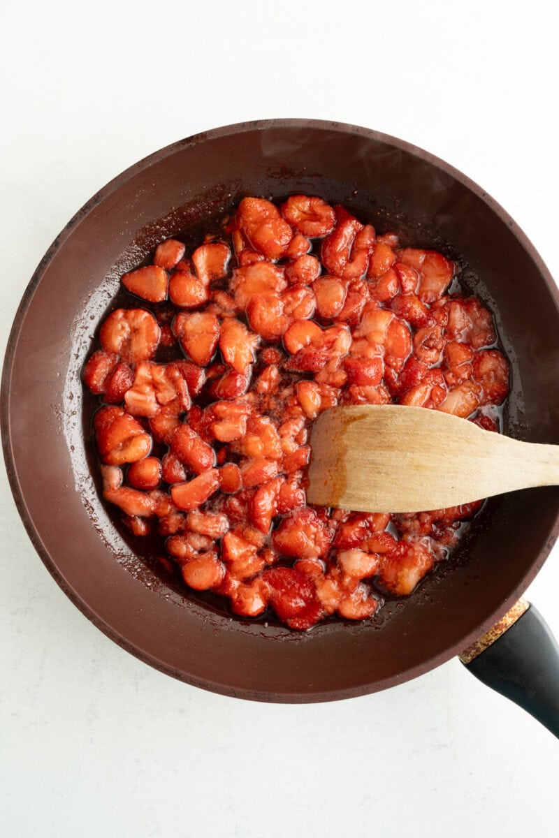 Cooked strawberries being macerated with a wooden spoon.