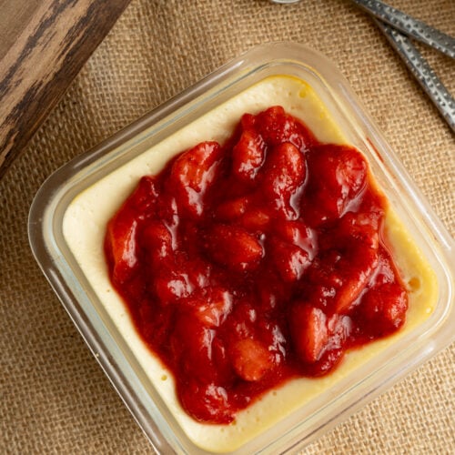 A single strawberry cottage cheese cheesecake cup on burlap with two spoons.