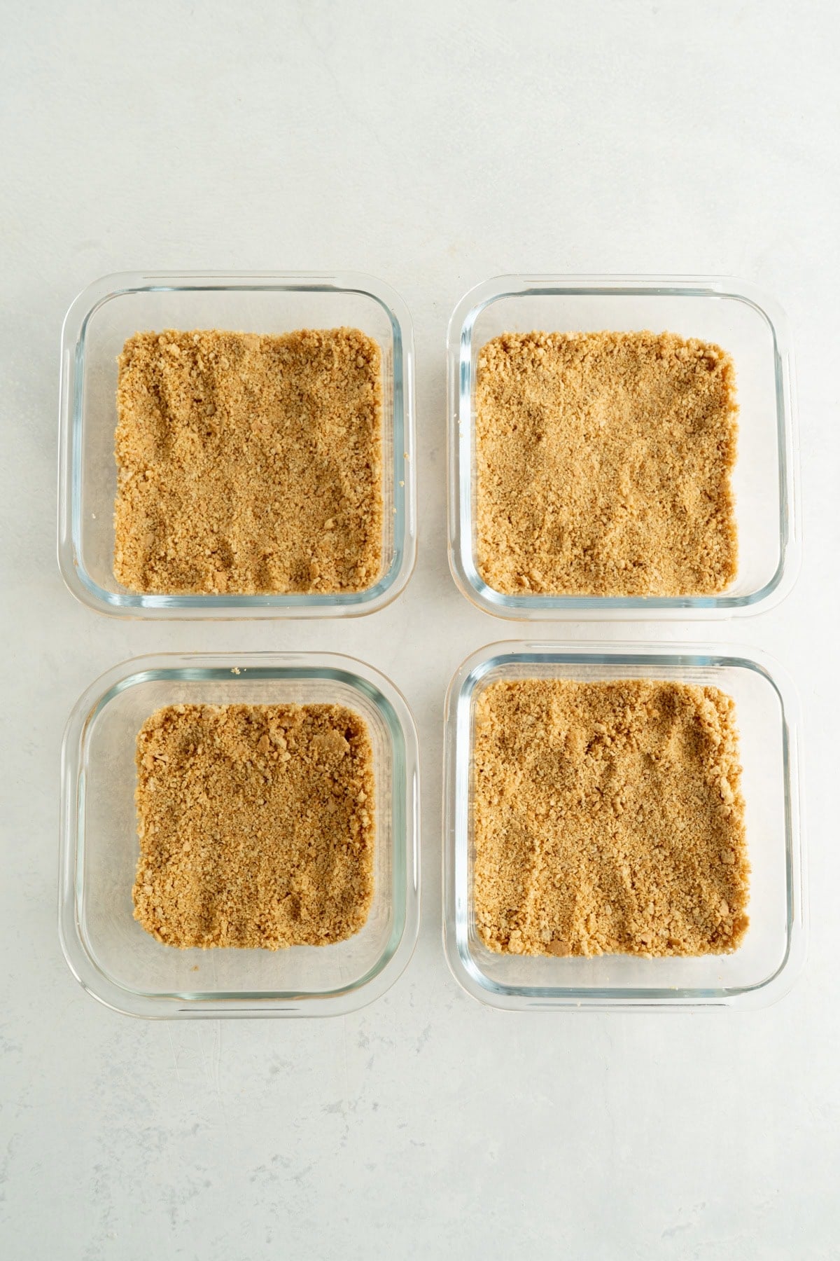Four single serving square dishes with graham crackers in the bottom.