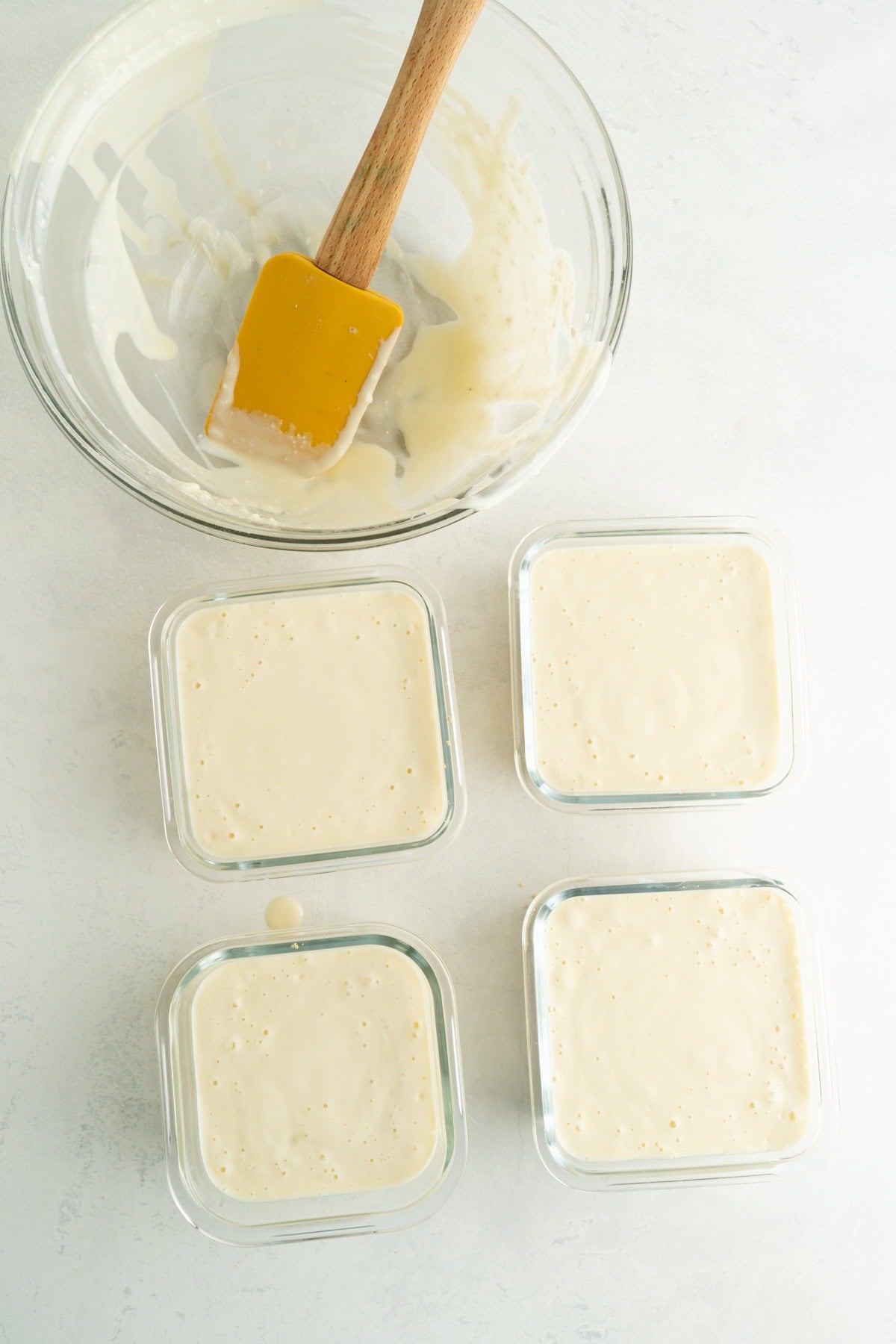 Four square glass small glass dishes filled with unbaked cheesecake filling.