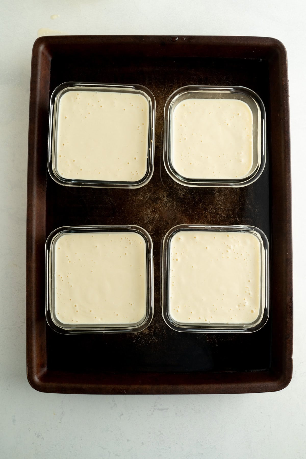 Four unbaked single serve cottage cheese cheesecakes on a baking sheet filled with water.