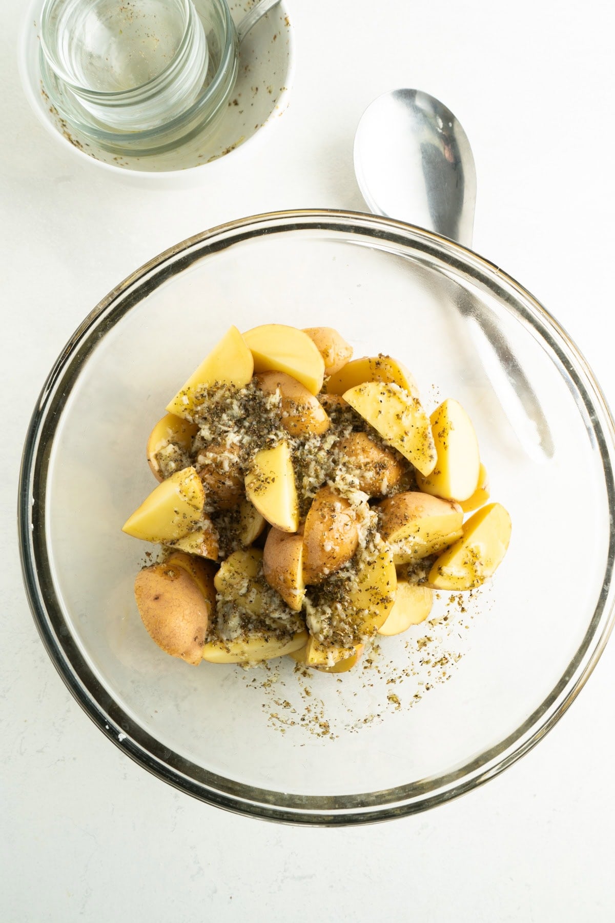 Potatoes in a bowl being so tossed in a Greek marinade.