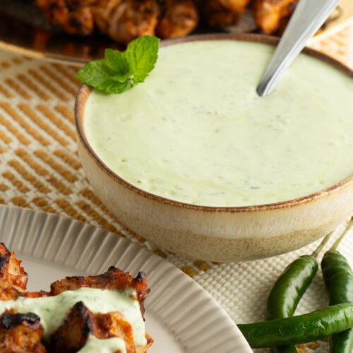 A bowl of mint yogurt sauce on a table with tandoori chicken.