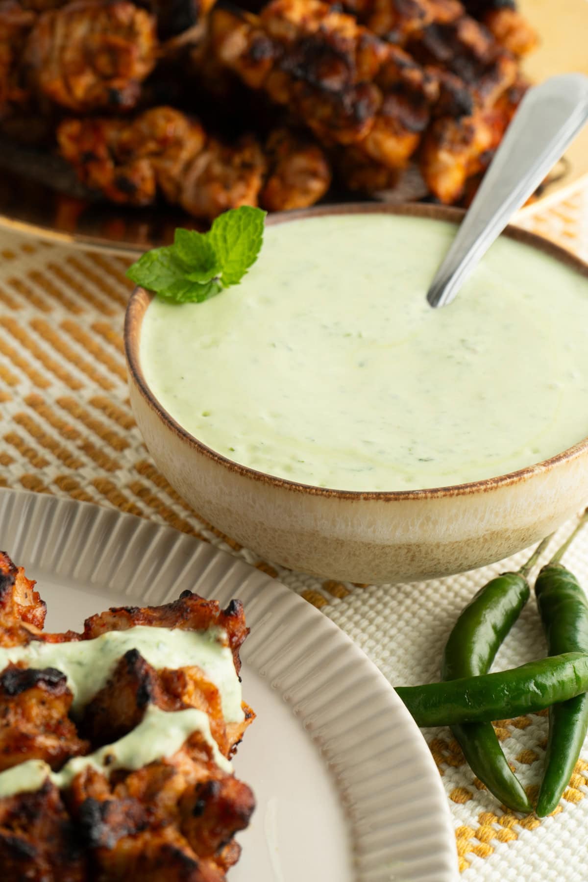 A bowl of mint yogurt sauce on a table with tandoori chicken.