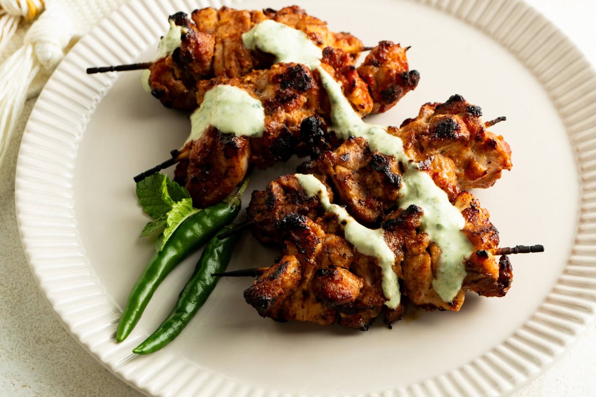 A plate of Tandoori Chicken Tikka topped with a drizzle of yogurt mint sauce.