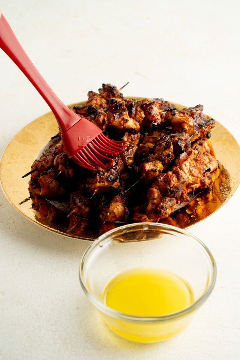 Chicken skewers being basted with butter.