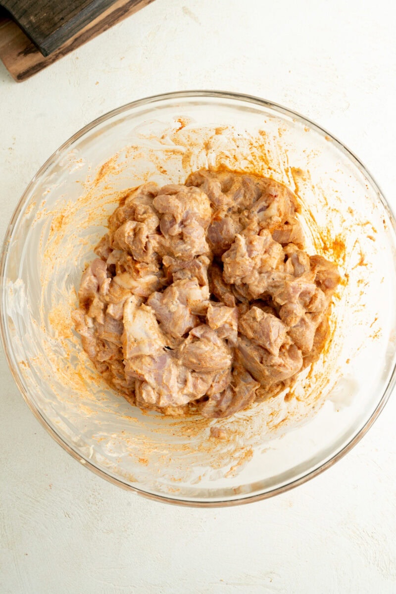 Cubed chicken thighs in a bowl with tandoori marinade.