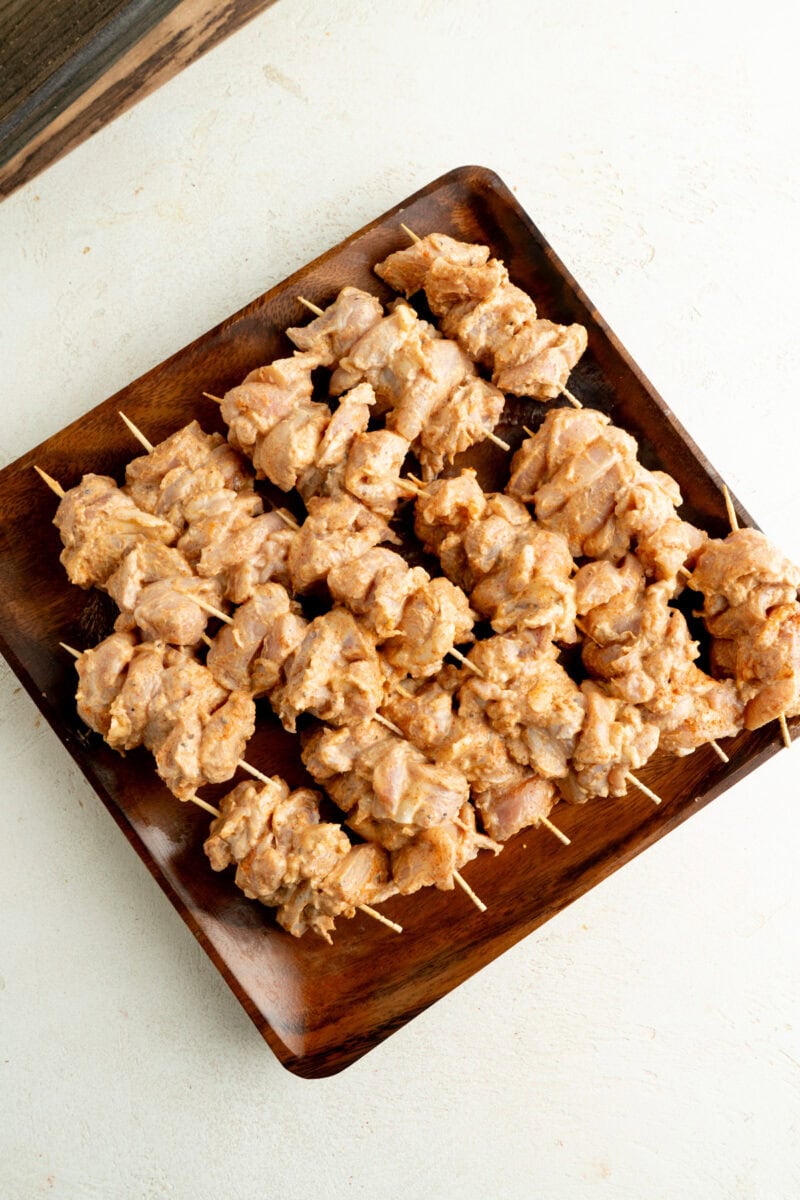 Small chicken skewers on a wooden plate.